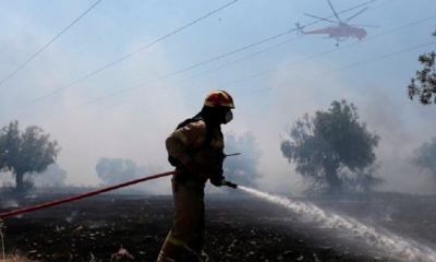 Un bombero rocía agua mientras un helicóptero de extinción de incendios Sikorsky S-64 opera, durante un incendio forestal 
