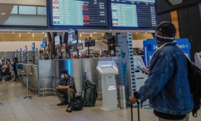 Un pasajero sostiene su teléfono móvil mientras mira un tablón de anuncios de vuelo electrónico que muestra vuelos cancelados 