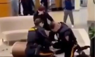 Los dos agentes esposan al afroamericano y lo mantienen contra el piso, mientras el joven blanco permanece sentado.