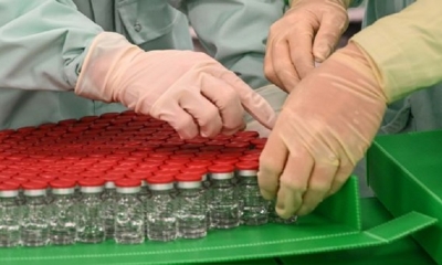 Técnicos de laboratorio manipulan viales tapados como parte de las pruebas de llenado y envasado para la producción y suministro a gran escala 