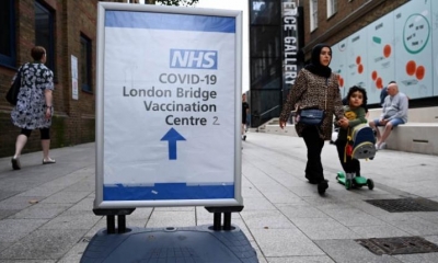 La gente pasa junto a un cartel de vacunación Covid fuera de un hospital en el centro de Londres, Gran Bretaña. | EFE