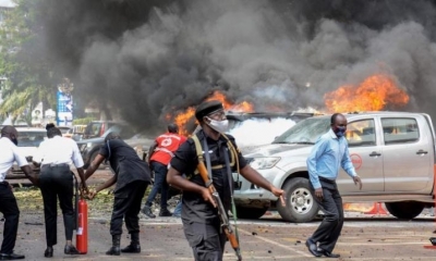 La gente apaga el fuego en los automóviles causado por la explosión de una bomba cerca del edificio del Parlamento en Kampala