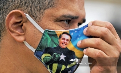 Una persona lleva un barbijo con la foto de Bolsonaro. / AFP