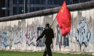 Un hombre pasa junto a una sección conservada del Muro de Berlín con una bandera soviética, este viernes 13. Fotos: AFP.